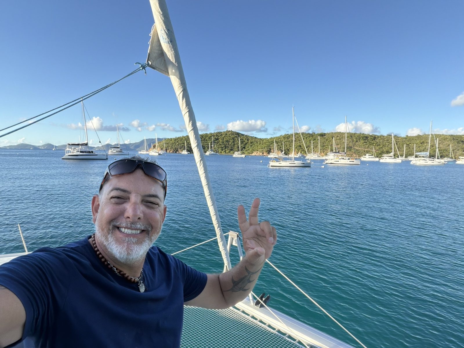 Clint Kendall aboard the catamaran on a sunny day, a British Virgin Islands anchorage full of moored sailboats behind him