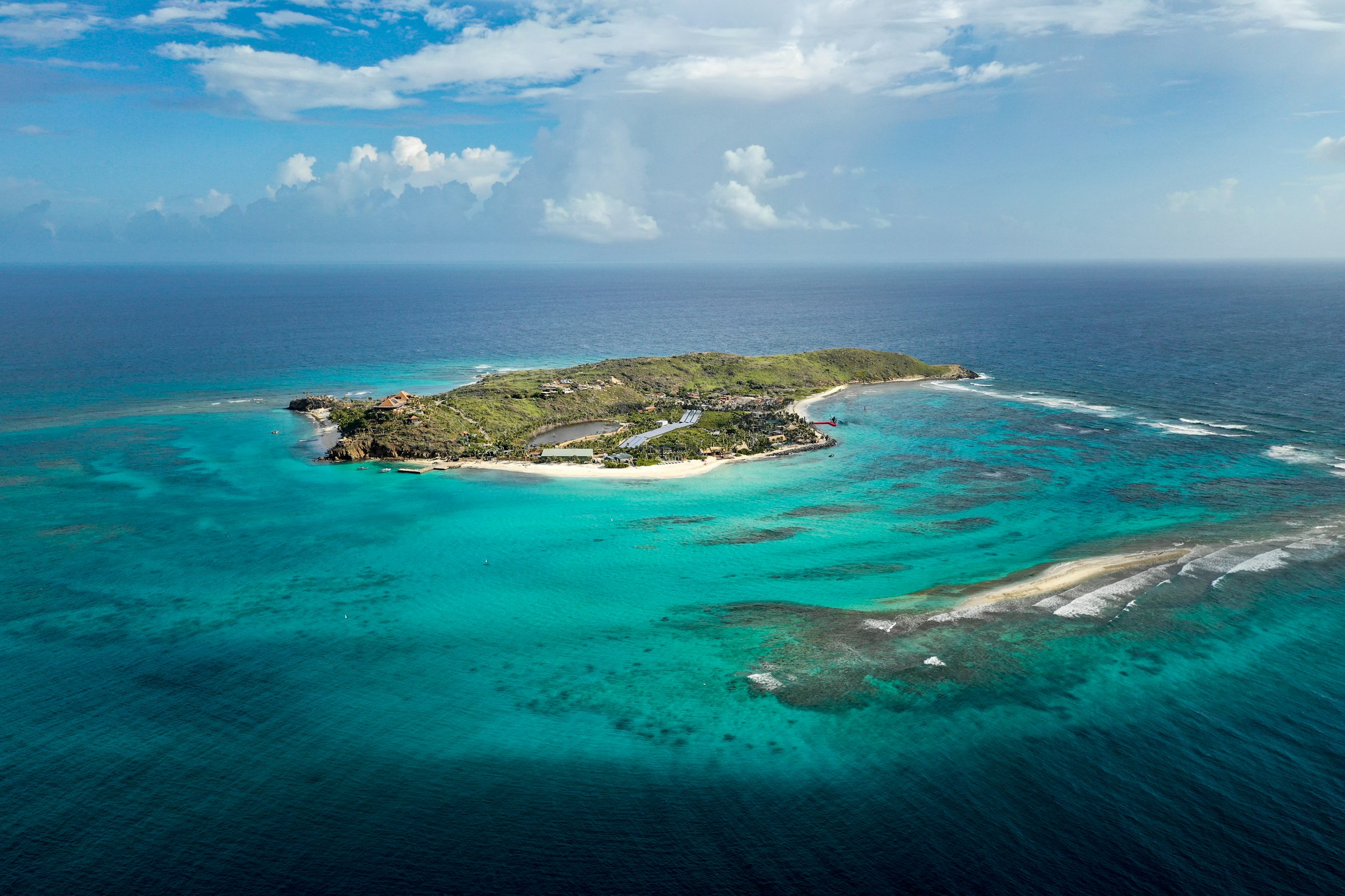 Aerial view of a small green island ringed by turquoise reef water in the British Virgin Islands